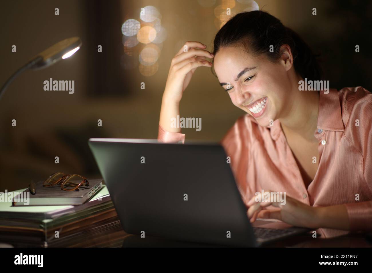 Tele worker in the night laughing checking laptop at home Stock Photo