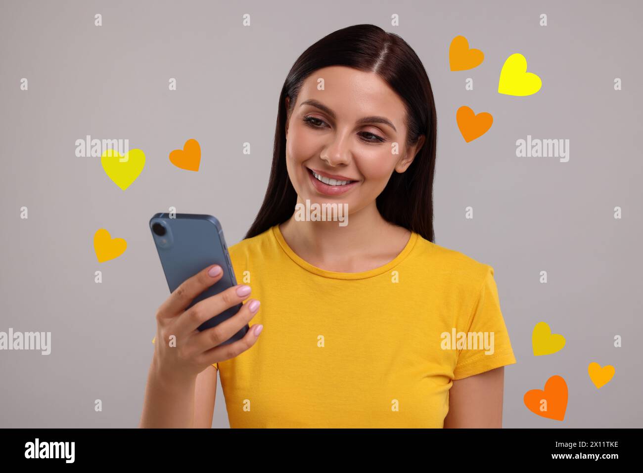 Long distance love. Woman chatting with sweetheart via smartphone on grey background. Hearts flying out of device and swirling around her Stock Photo