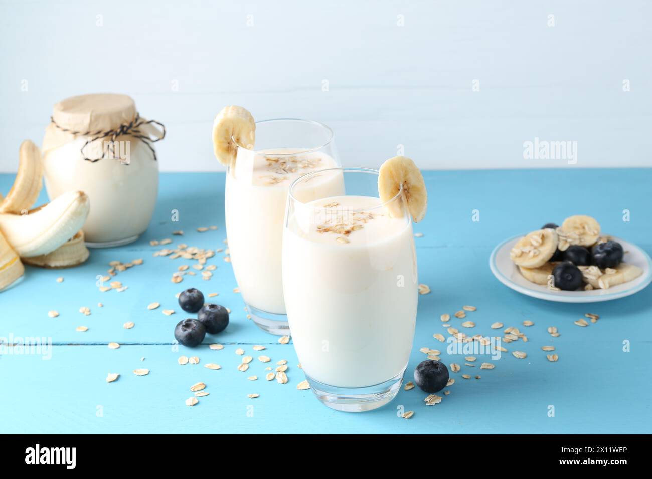 Tasty yogurt in glasses, oats, banana and blueberries on light blue wooden table Stock Photo
