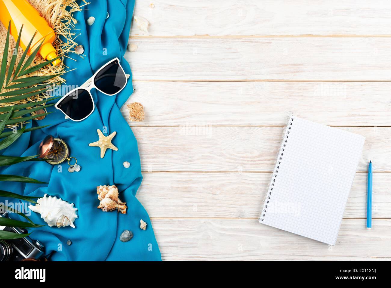 Vacation planning background of notebook seashells, starfish, sunglasses, compass, camera and straw hat on blue fabric and white planks flat lay with Stock Photo