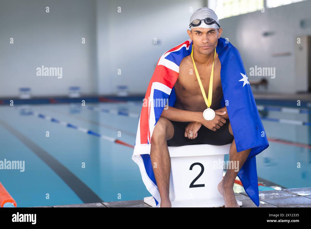 Male athlete swimmer wrapped in Australian flag sitting on podium with gold medal Stock Photo
