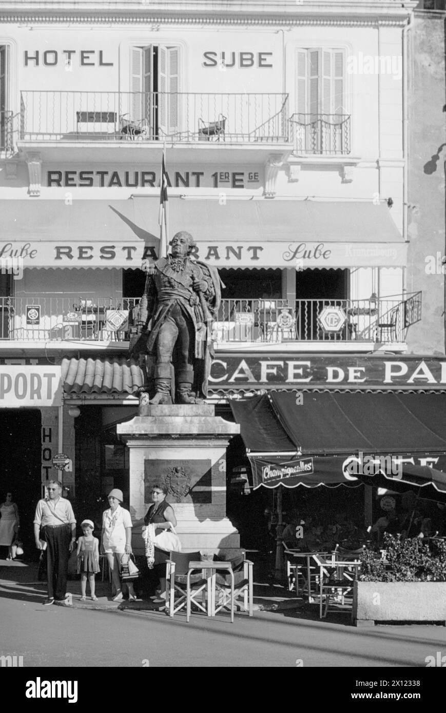 Tourists Outside Hotel Sube, Restaurant Sube and Cafe de Paris, Standing Next to Statue of Admiral Pierre André de Suffren of Saint Tropez, Quai Suffren, Old Port, Saint Tropez, Côte d'Azur, France. Vintage or Historic Image c1960 Stock Photo