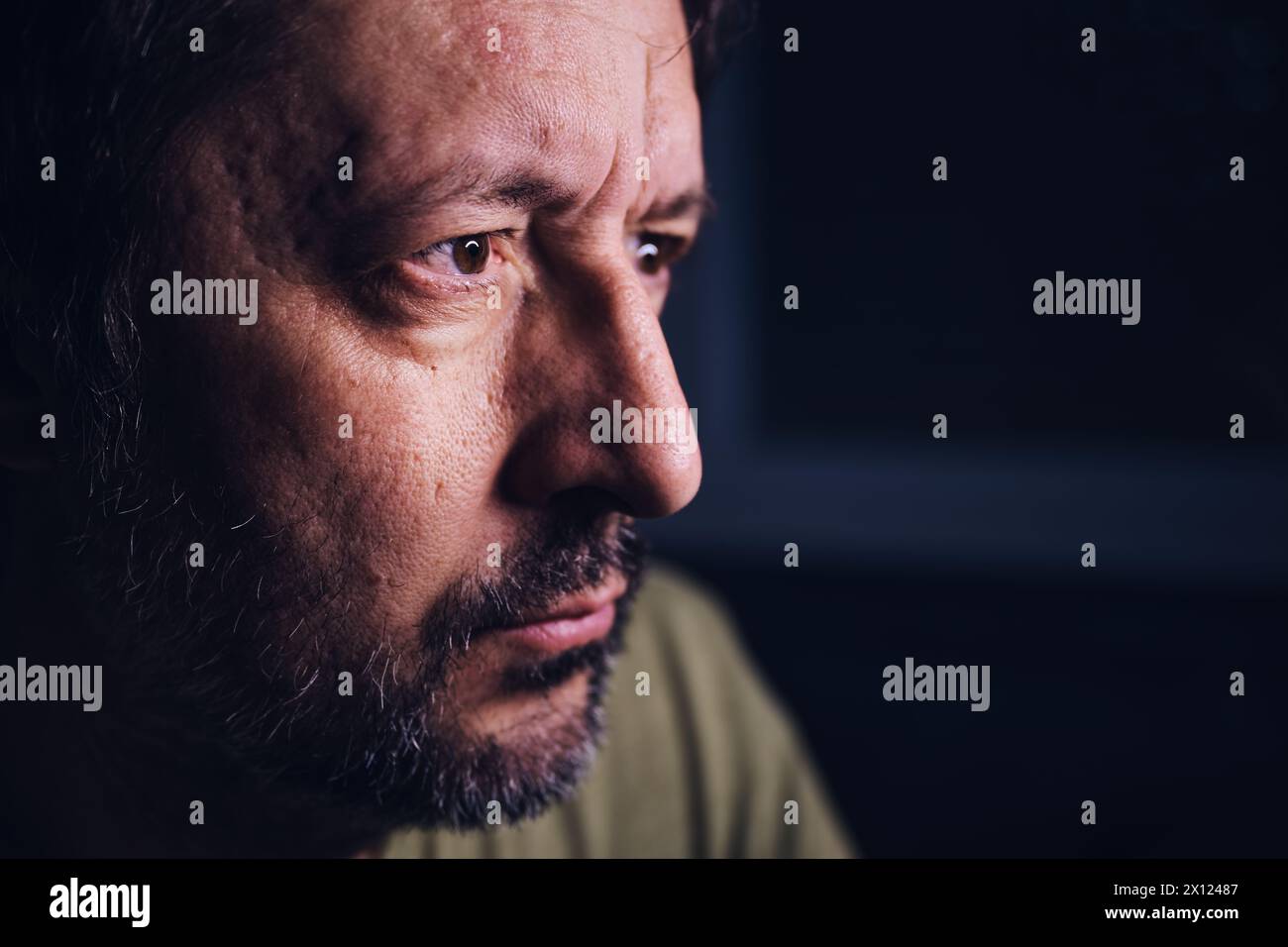 Concerned man, portrait of adult male looking at device screen at night, hearing bad news on television, low key with selective focus Stock Photo