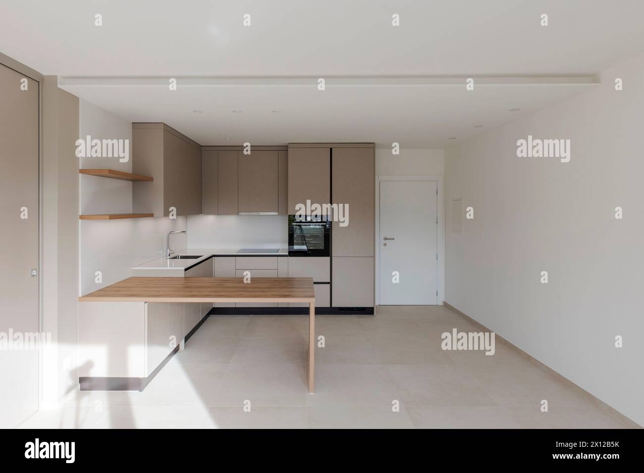 Front view of a new kitchen with a sturdy wooden table in front. Very large space or room with white walls. Stock Photo