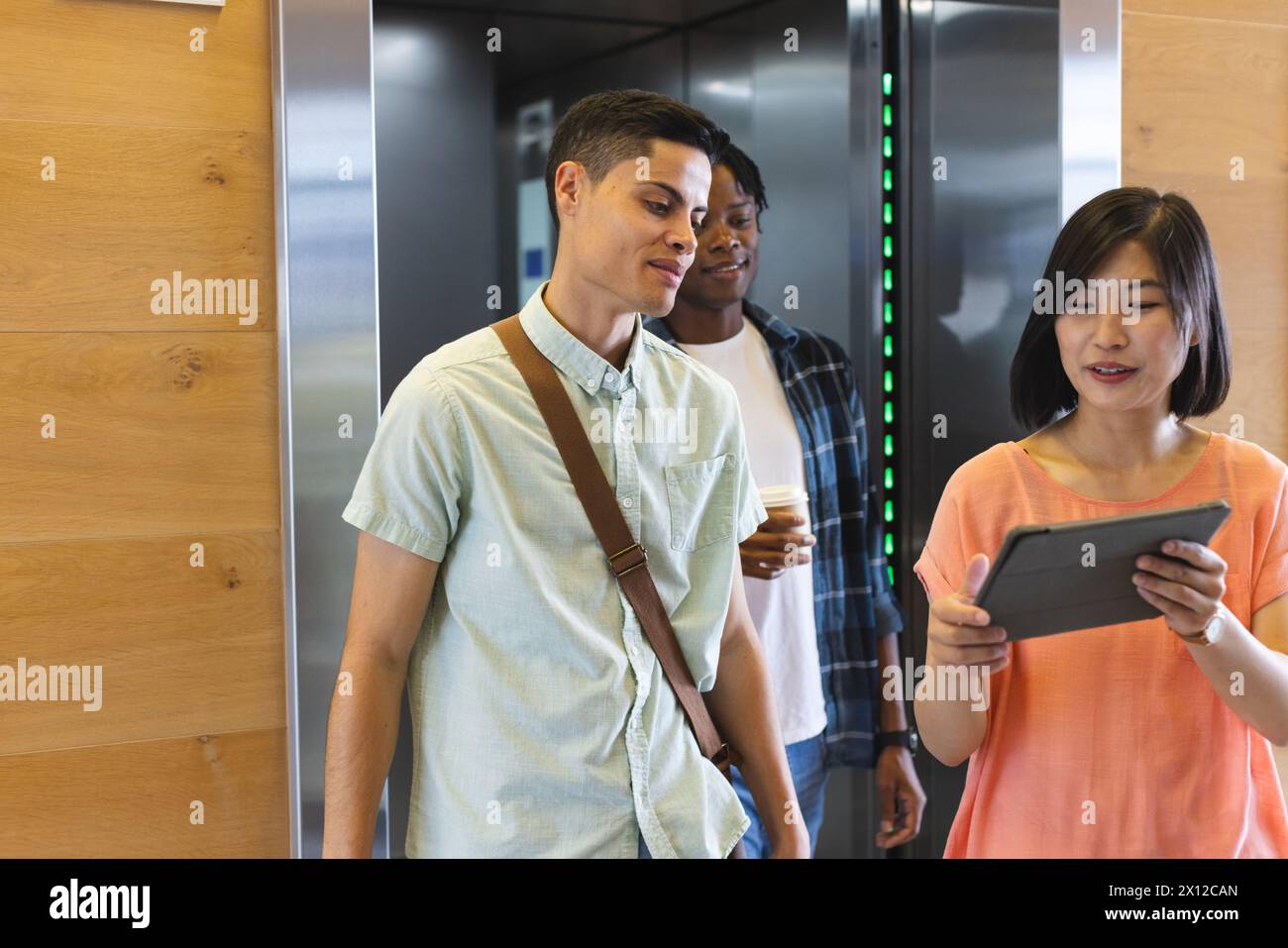 Diverse group of colleagues standing in elevator in a modern business office, looking at tablet Stock Photo