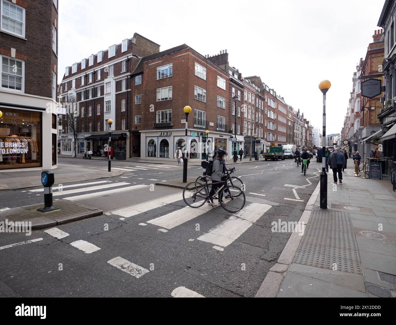 Marylebone high street London with retail shops and  stores with cyclists on  pedestrian crossing in  foreground Stock Photo