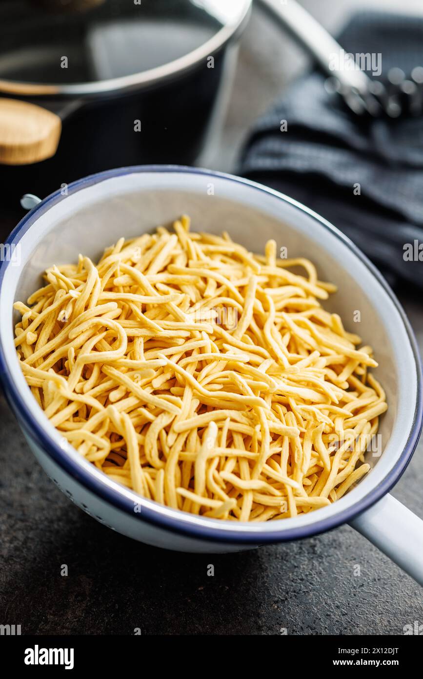 Uncooked spaetzle pasta in colander on a kitchen table. Stock Photo