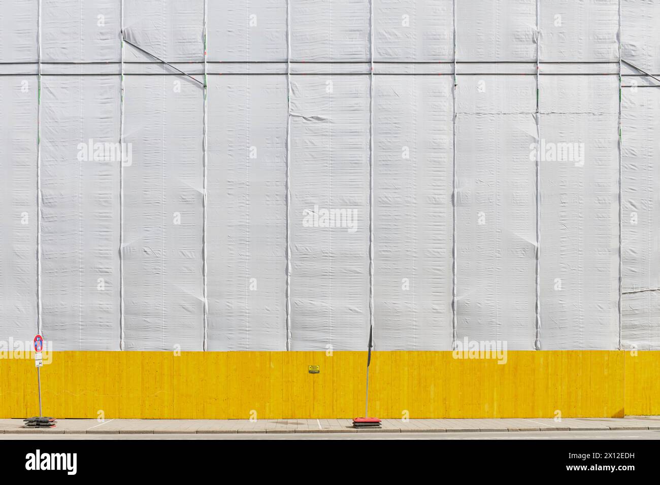 Wegen Bauarbeiten abgehängte Fassade mit gelbem Bauzaun im hellen Sonnenschein Stock Photo