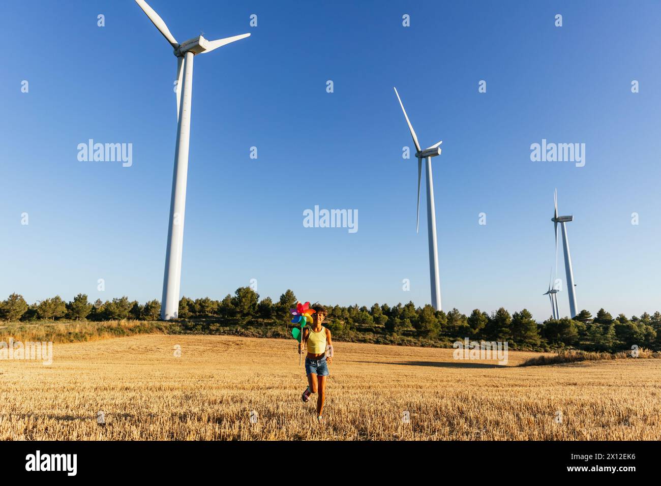 Sweet girl runs through a field with a colorful pinwheel in her hand ...