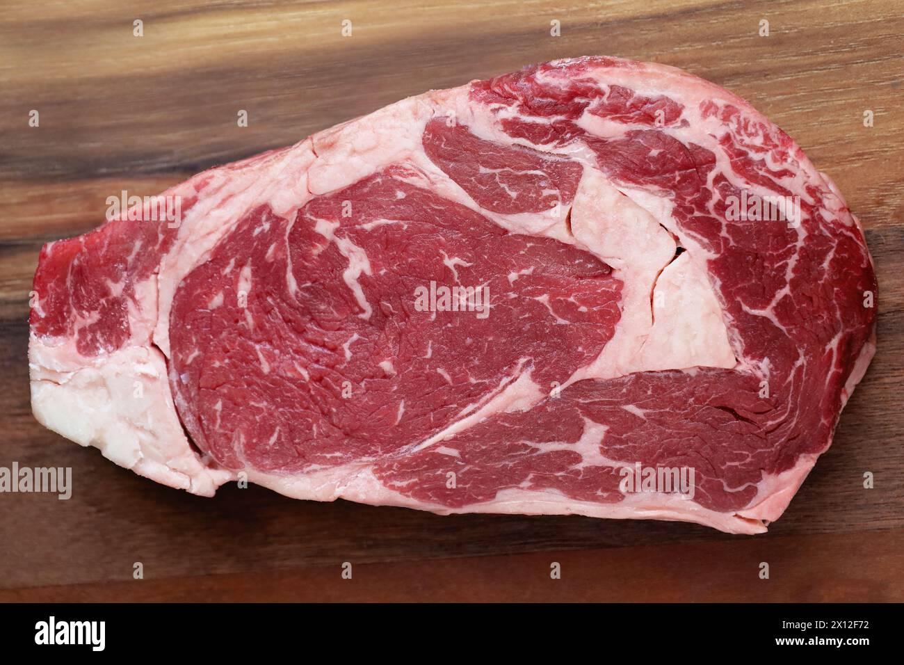 A raw marbled ribeye steak on a cutting board Stock Photo