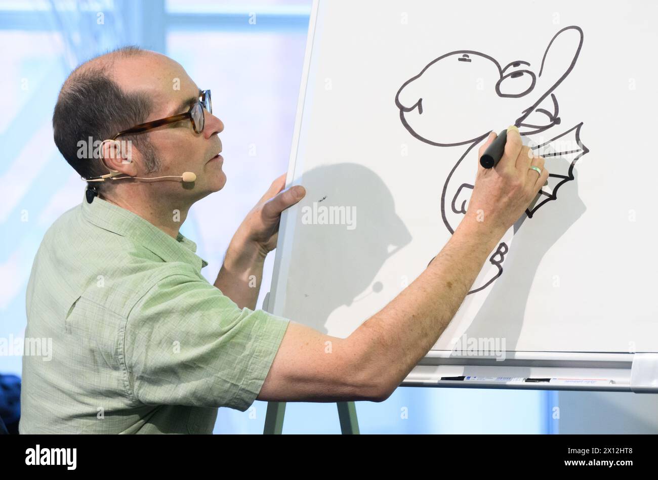 Hanover, Germany. 15th Apr, 2024. Children's book author Ingo Siegner draws his book character Dragon Coconut at a reading for primary school children at the Künstlerhaus Hannover. To mark the 70th anniversary of the Friedrich-Bödecker-Kreis Niedersachsen (FBK), 70 readings by authors for nurseries and schools in Lower Saxony are taking place. Children's book author Ingo Siegner read from his Dragon Coconut books. Credit: Julian Stratenschulte/dpa/Alamy Live News Stock Photo
