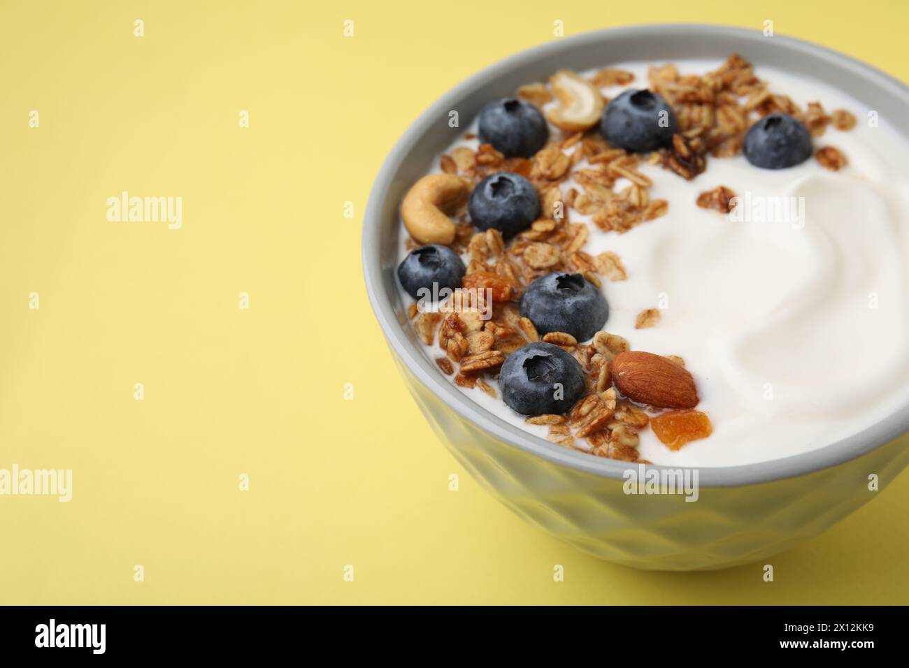 Bowl with yogurt, blueberries and granola on yellow background, closeup. Space for text Stock Photo