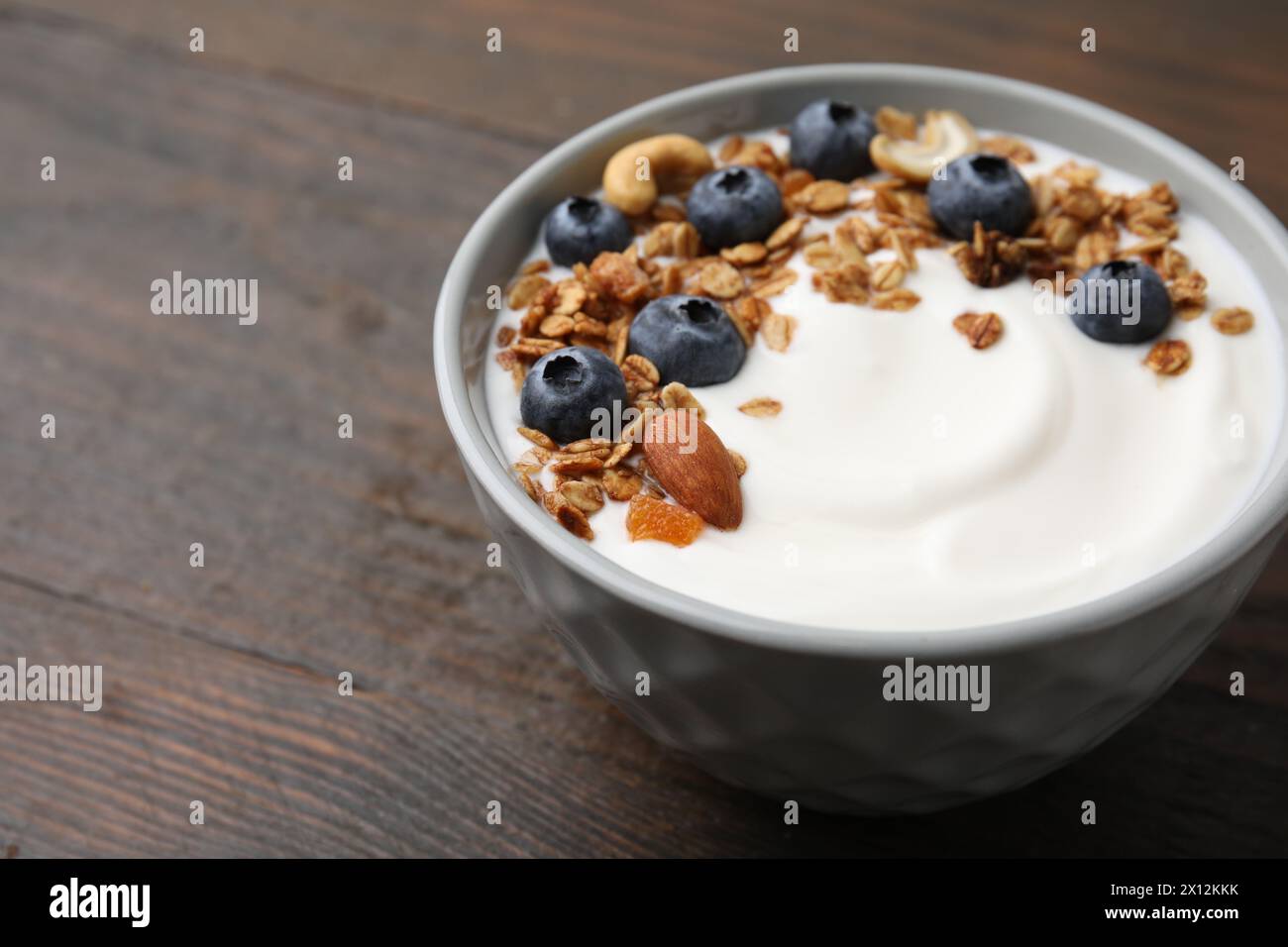 Bowl with yogurt, blueberries and granola on wooden table, closeup. Space for text Stock Photo