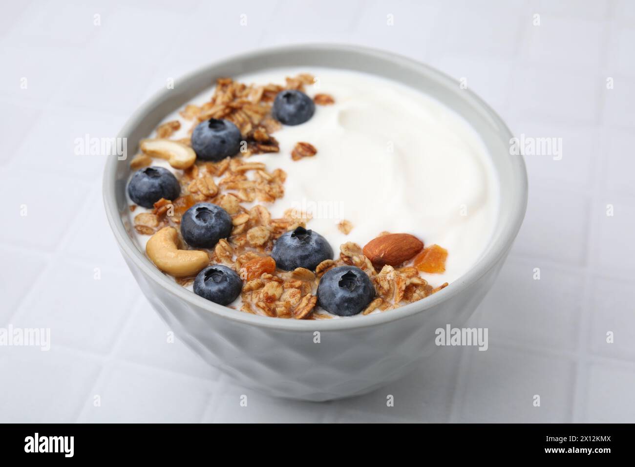 Bowl with yogurt, blueberries and granola on white tiled table, closeup Stock Photo