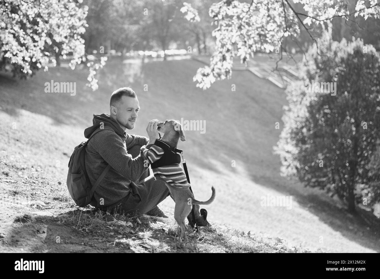 man with his cute puppy in a sweater in the park training, feeding, smiling. Spring, summer, autumn handsome man having fun with his dog outdoor. Space for text. High quality photo Stock Photo