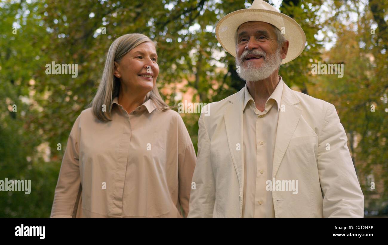Happy Caucasian grandparents retired pair pensioners smiling woman man stroll together talk retirement outdoors city nature park. Joyful elderly Stock Photo