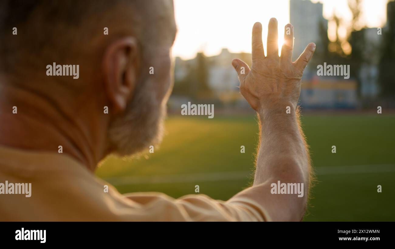Elderly man sportsman athlete sportive looking fingers hand sun rays training warm-up recreation healthcare physical active stadium bodycare Stock Photo