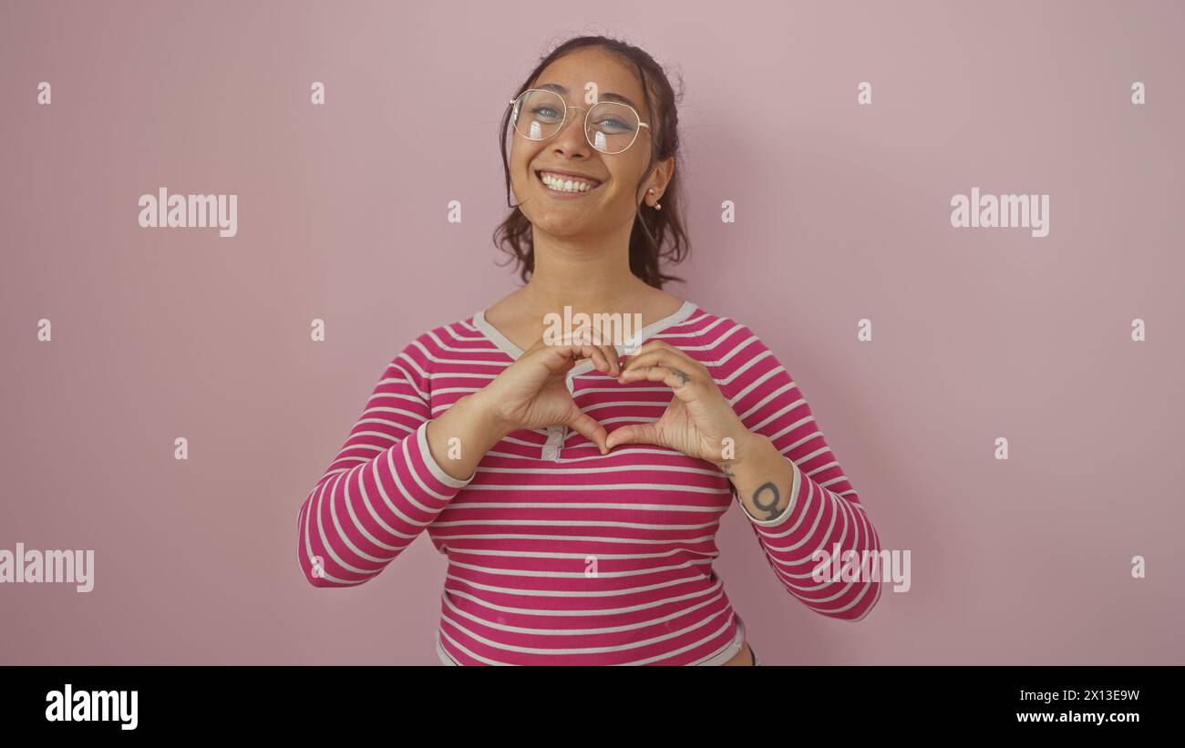 A cheerful young woman makes a heart shape with her hands against a ...
