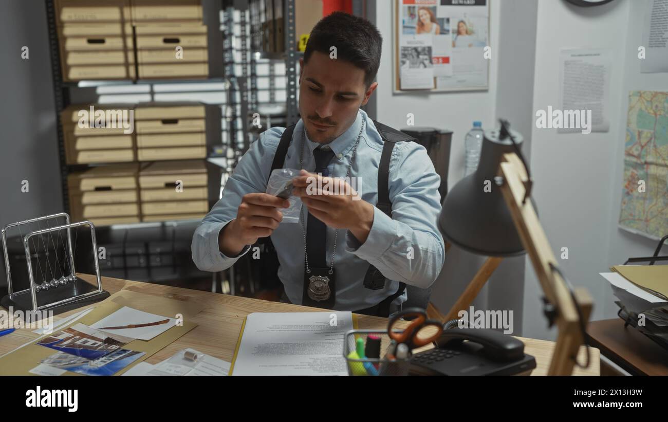 A focused young hispanic man with a beard, wearing a detective badge, examines evidence in a police department office. Stock Photo
