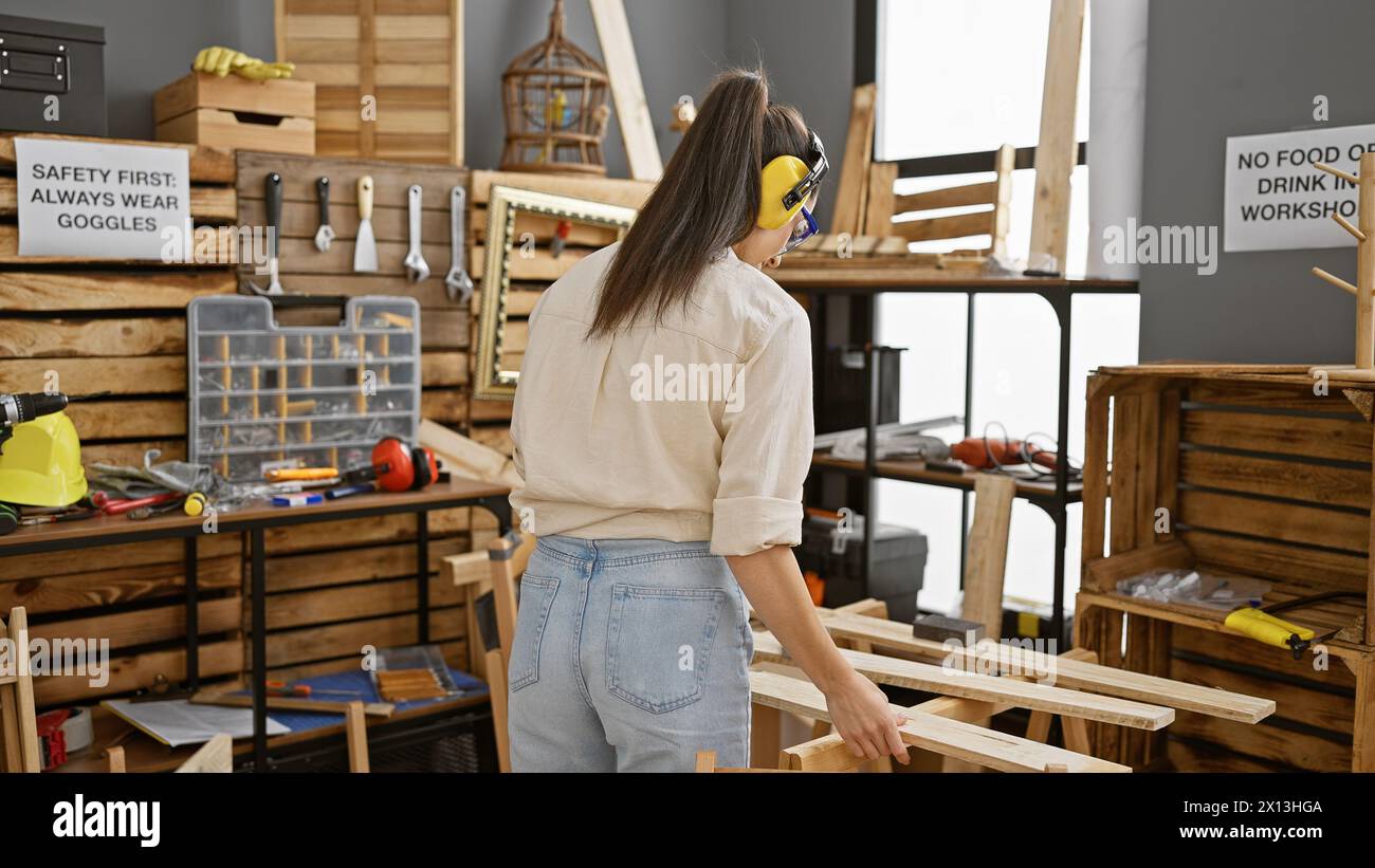 Radiant young hispanic woman carpenter savours the sweet sound of woodworking, adorned in headphones at her carpentry workshop Stock Photo