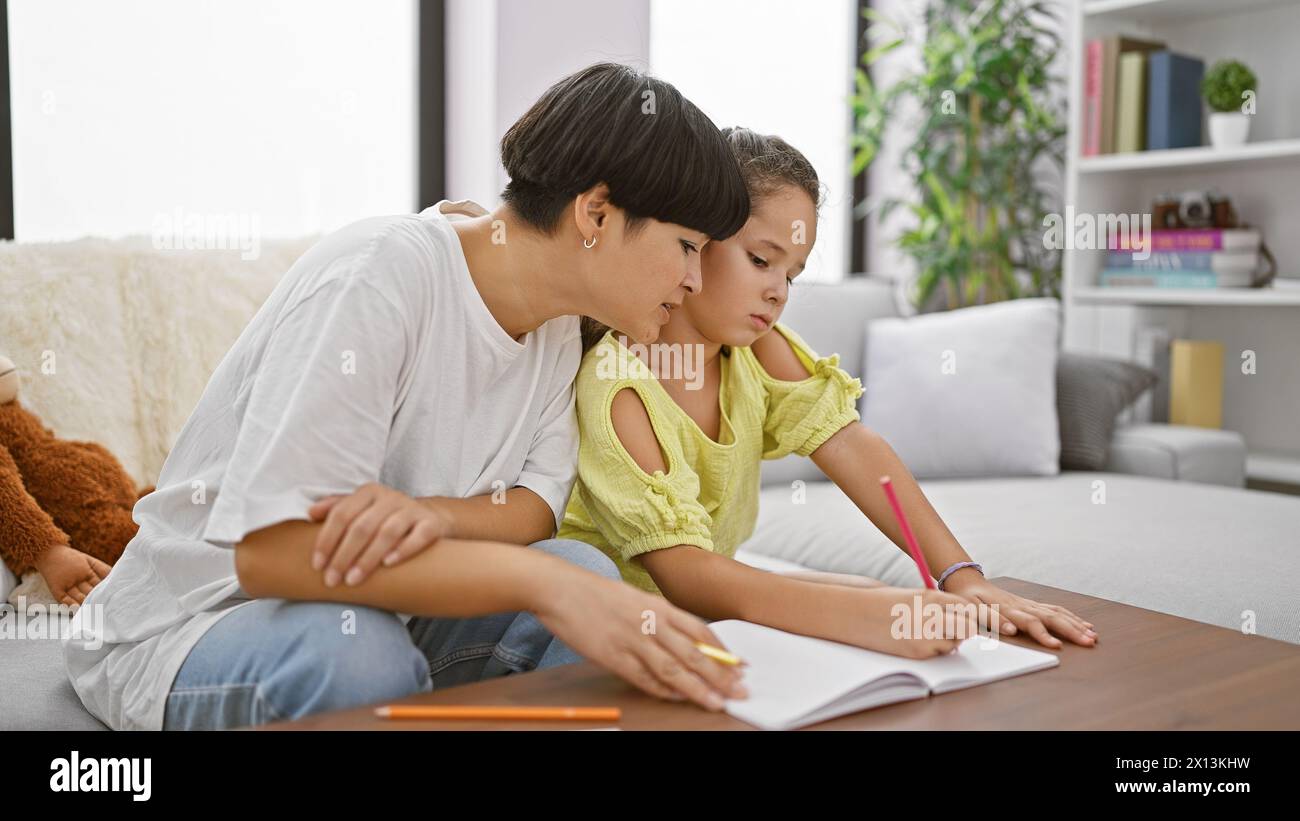 Relishing mother-daughter bond, sitting together at home, drawing intimate expressions on notebook in the quietude of their living room Stock Photo