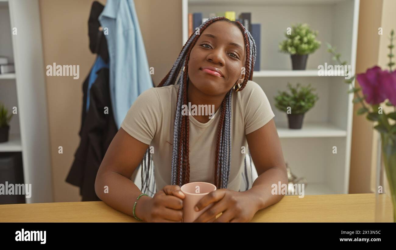 An african woman with braids smiles while holding a cup in a cozy ...