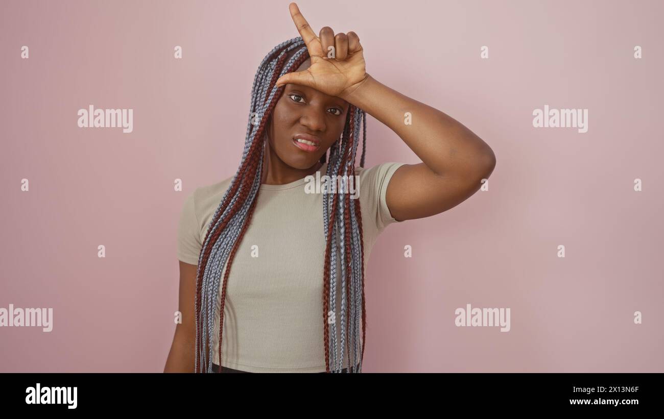 A playful african american woman with braids poses against a pink ...