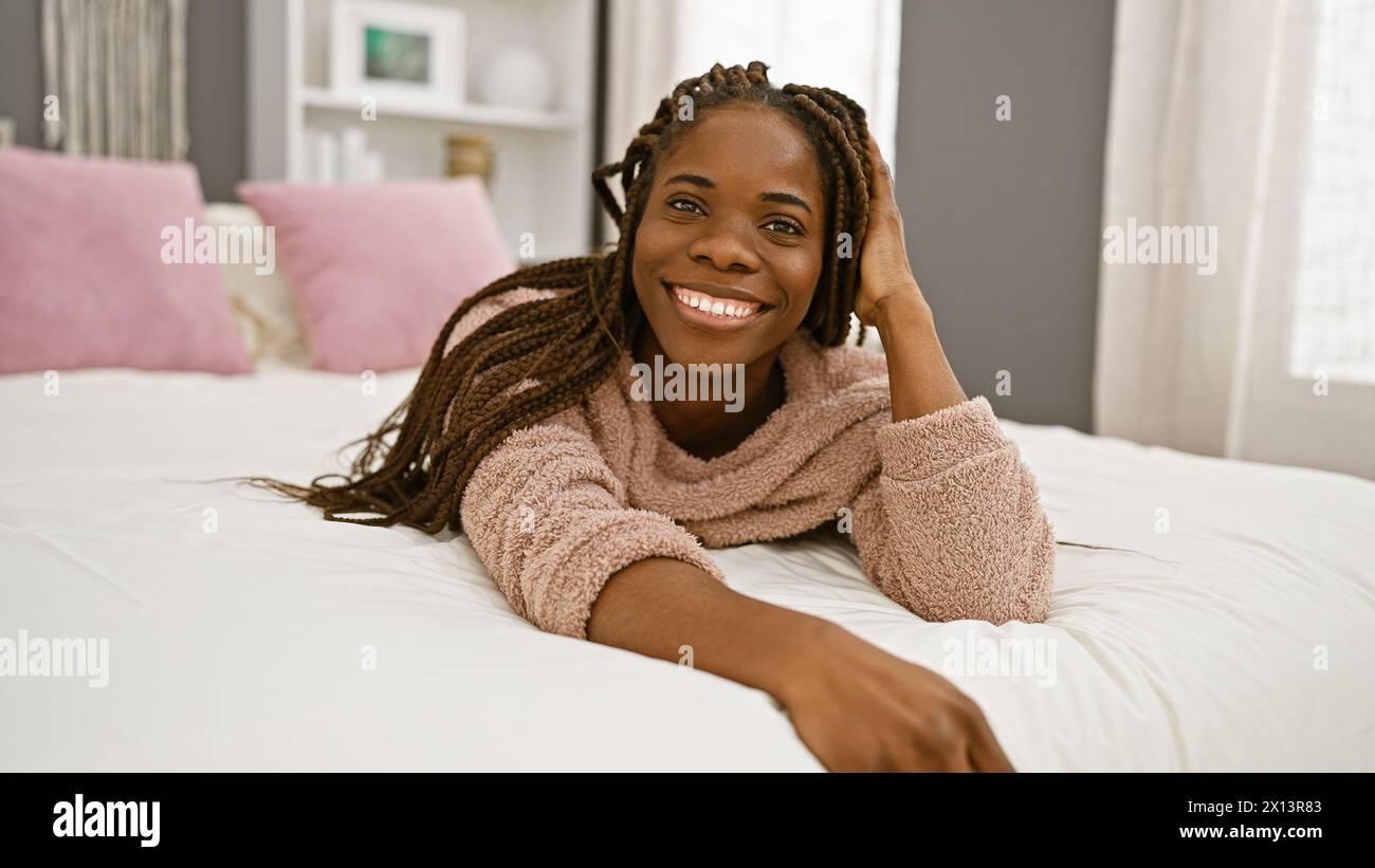 A smiling african woman with braids lying down in a cozy bedroom ...