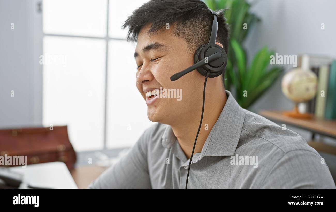 Smiling asian man with headset working in a modern office expressing approachability and professionalism. Stock Photo