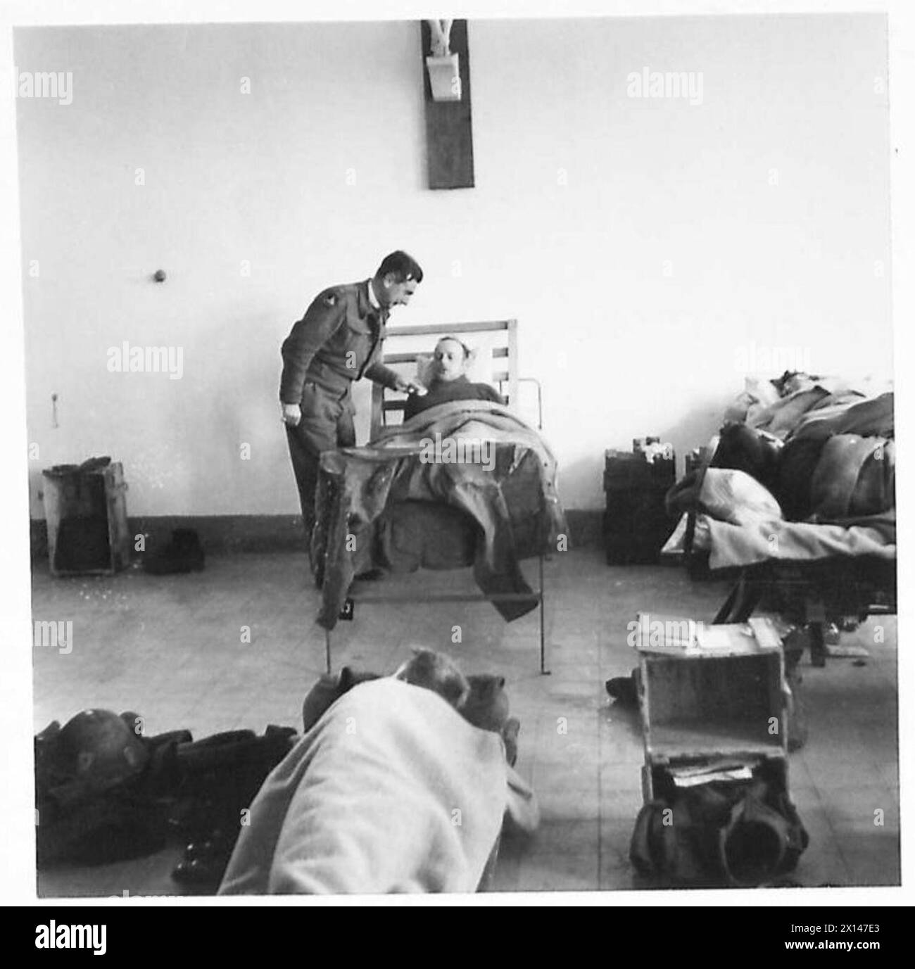 A CASUALTY CLEARING STATION AT WORK IN NORTH AFRICA - German casualties receive the same treatment as our own men. This prisoner - Fritz Ruehn - of the Africa Corps, occupies a bed in one of the wards after having two bullets removed, he is talking to The Rev. C.T.F. Thomas, one of the resident Padres British Army Stock Photo