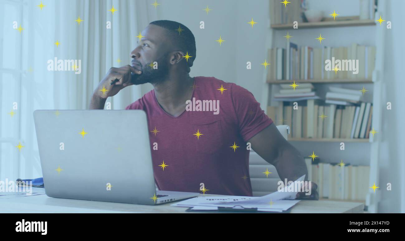 Image of shining star icons over african american man holding a document using laptop Stock Photo