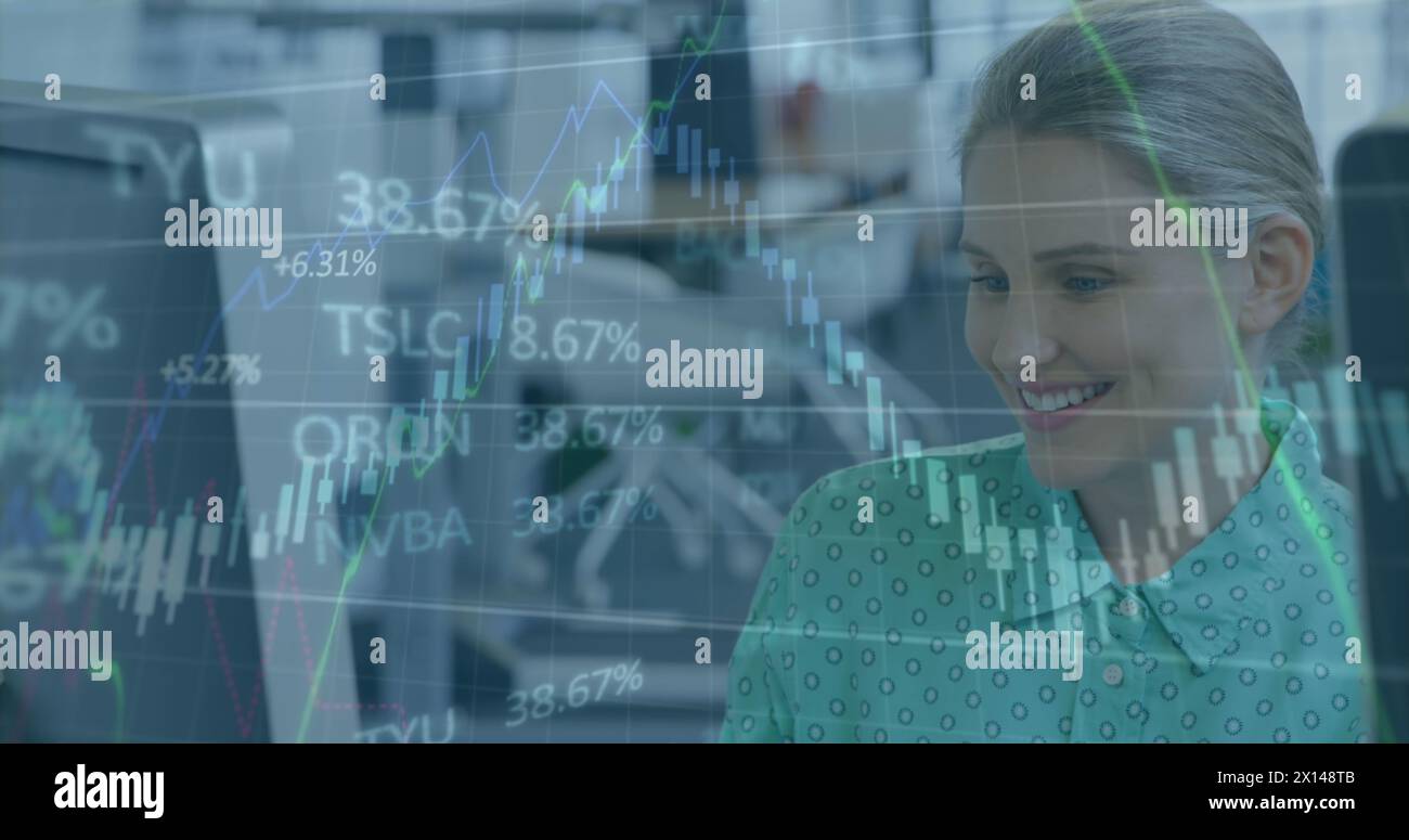 Image of graphs, trading board, caucasian woman talking with coworker while working on computer Stock Photo