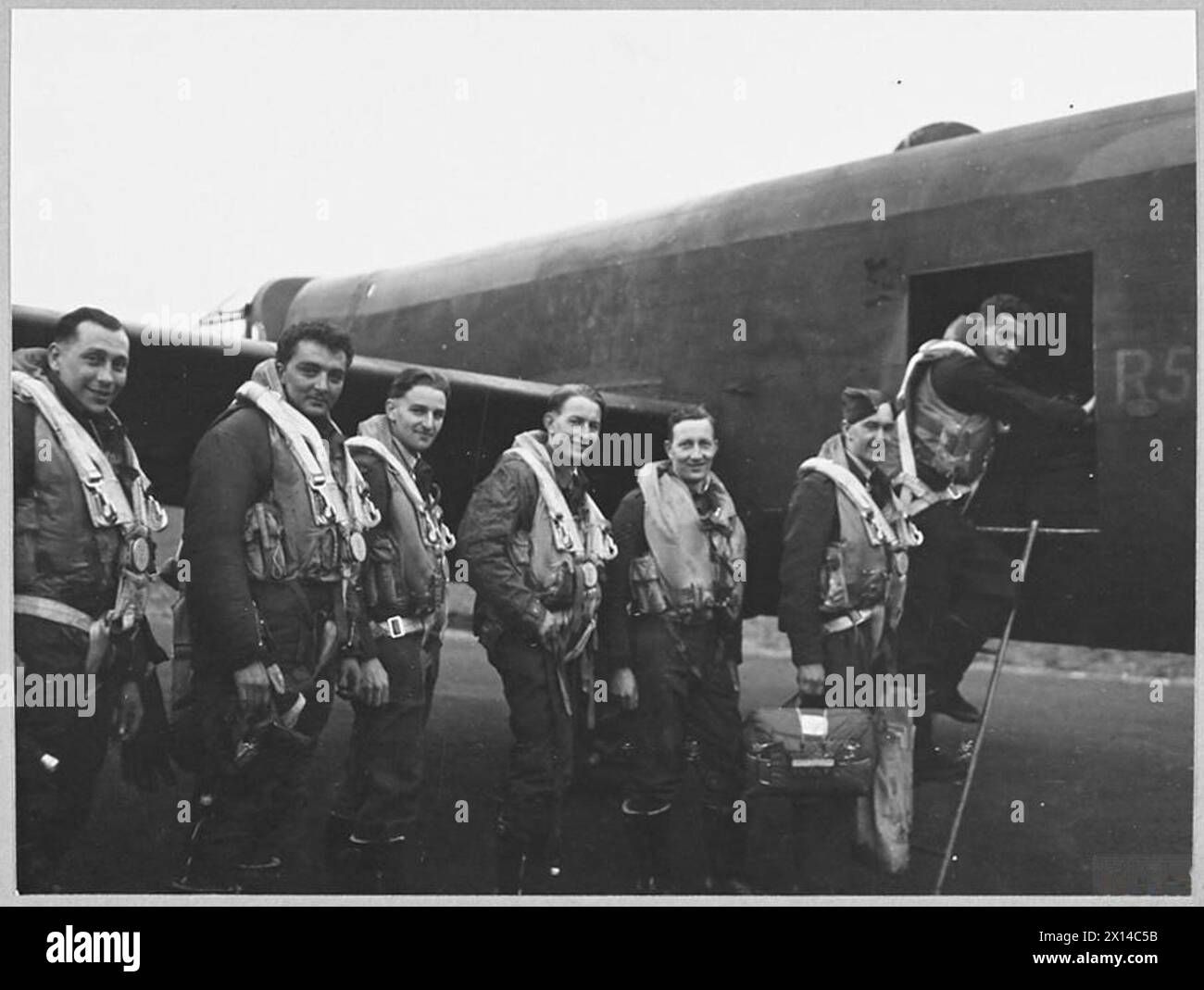 'S' FOR SUGAR COMPLETES ITS 100TH 'OP' - 13144 Picture (issued 1944) shows - The crew of 'S' for Sugar boarding the aircraft before the take off on the aircraft's 100th flight. They include Pilot Officer T.N. Scholefield of Australia, Flying Officer I. Hamilton of Glasgow, Flight Sergeant F.E. Hughes of Australia, Flight Sergeant R. Hillas of Australia, Flight Sergeant K. Stewart of Australia, Sergeant J. D. Wells of Sidcup, Kent, and Sergeant R.H. Burgess of Chester Royal Air Force Stock Photo