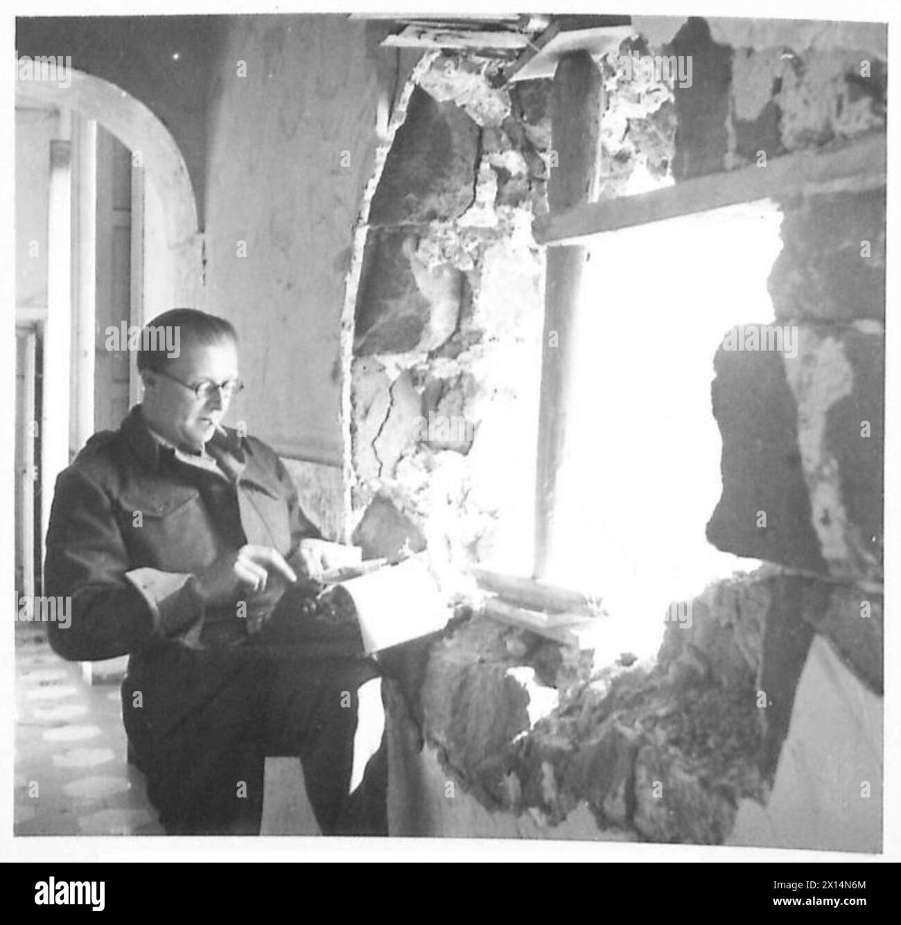 THE BRITISH ARMY IN NORTH AFRICA, SICILY, ITALY, THE BALKANS AND AUSTRIA 1942-1946 - Norman Smart of the Daily Express uses a wall as cover and the shored-up shellhole in the wall for observation purposes British Army Stock Photo