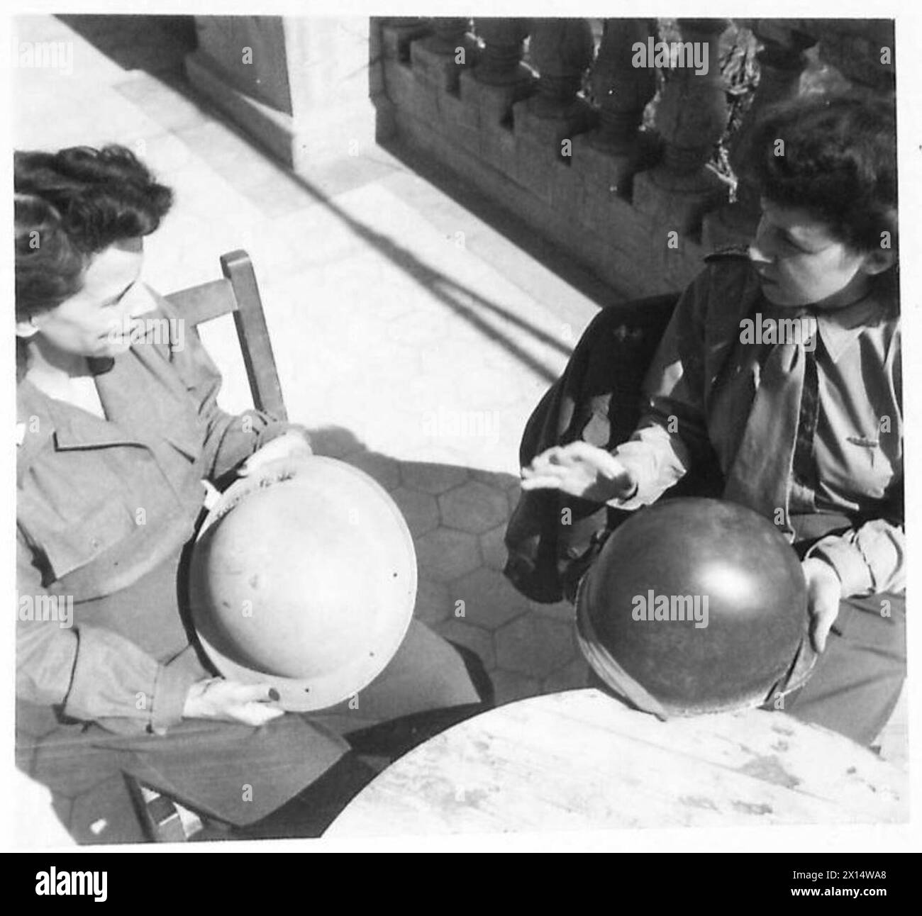 FIFTH ARMY - ANZIO BRIDGEHEAD SISTERS-IN-ARMS - All girls wear slacks and issue shirts, and the greatest difference in uniform is the steel helmet, which all troops and nurses on the bridgehead are compelled to wear regularly. 2/Lieut. Shuttack and Sister Daly swap helmets and examine the different types British Army Stock Photo