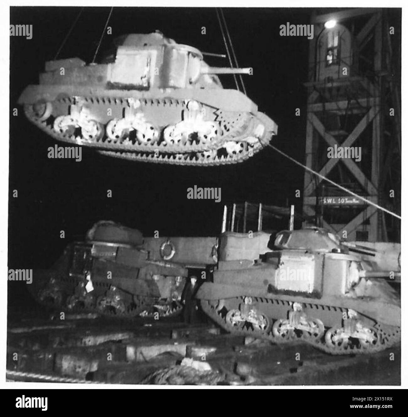 General Grant tanks are unloaded day and night from a ship using a floating crane, illustrating military logistics and armored vehicle deployment by the British Army. Stock Photo
