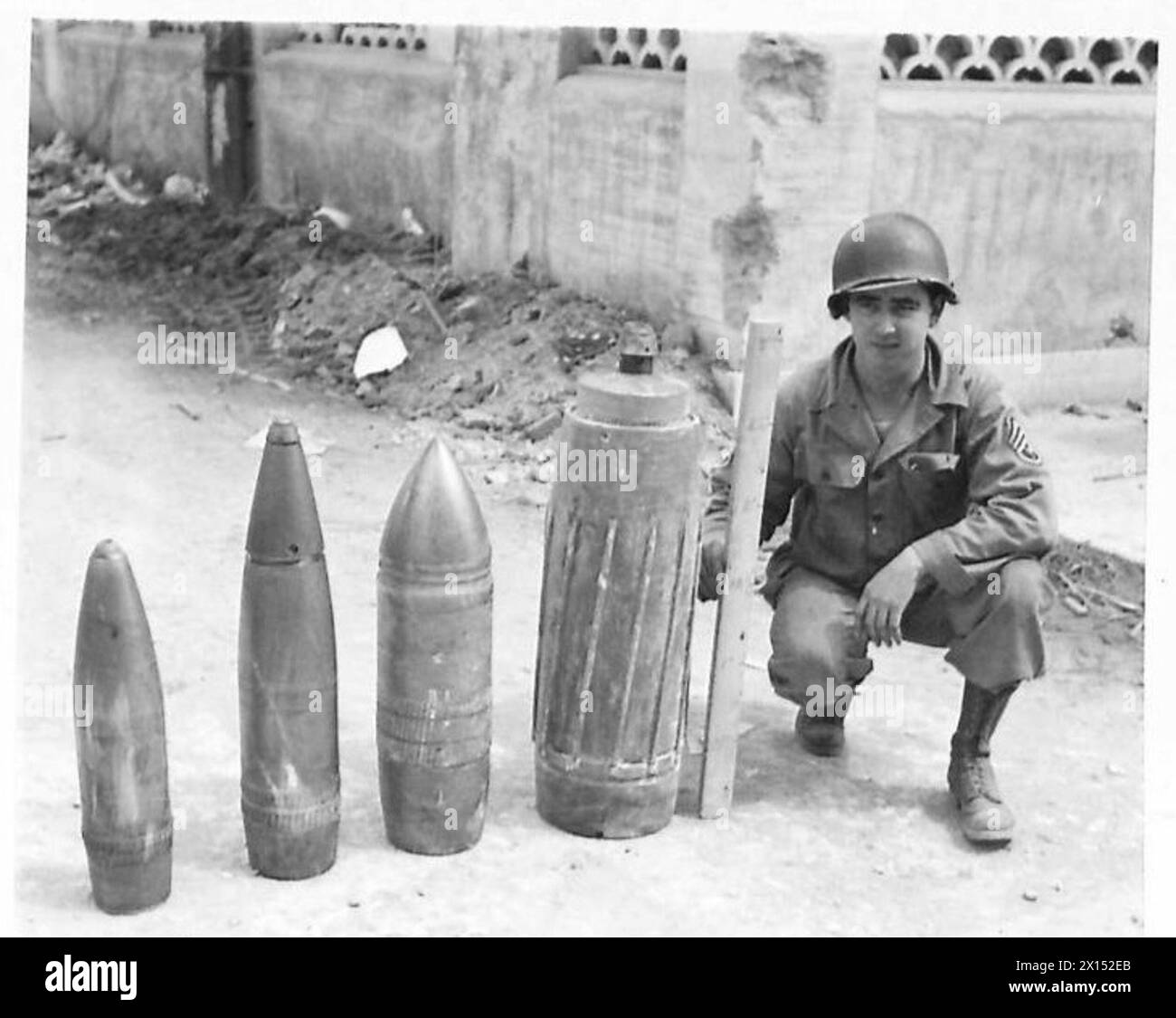 FIFTH ARMY : ANZIO BRIDGEHEAD COMPARISON IN GERMAN SHELLS - Four German shells that have been recovered on the bridgehead. Left to right: - 150 mm - 6 inch 180 mm - 7.2 inch 210 mm - 8.4 inch 280 mm - 11.2 inch 1st Sgt. William A. Hill of Charlestown, S.C., U.S.A. holds up a stick marked off in 6-inch lengths to give an idea of the size of the shells. The 280 mm shell has a mose-cap which is estimated to add 24' to its length. Round the body of the shell are raised strips which fit into the rifling of the gun barrel, the gas seal being obtained by a narrow copper band at the base end of the ra Stock Photo