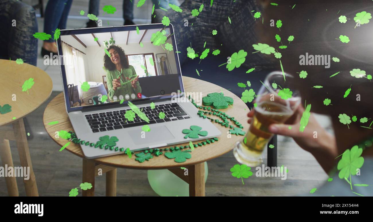 Clover leaves falling against woman drinking beer while having a image call on laptop at a bar Stock Photo