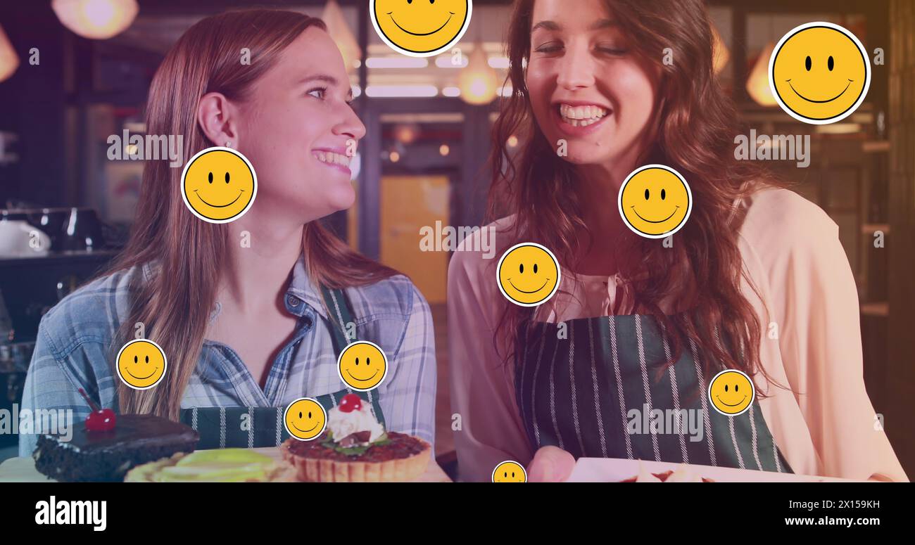 Image of emoticons over happy caucasian female bakers with cakes Stock Photo