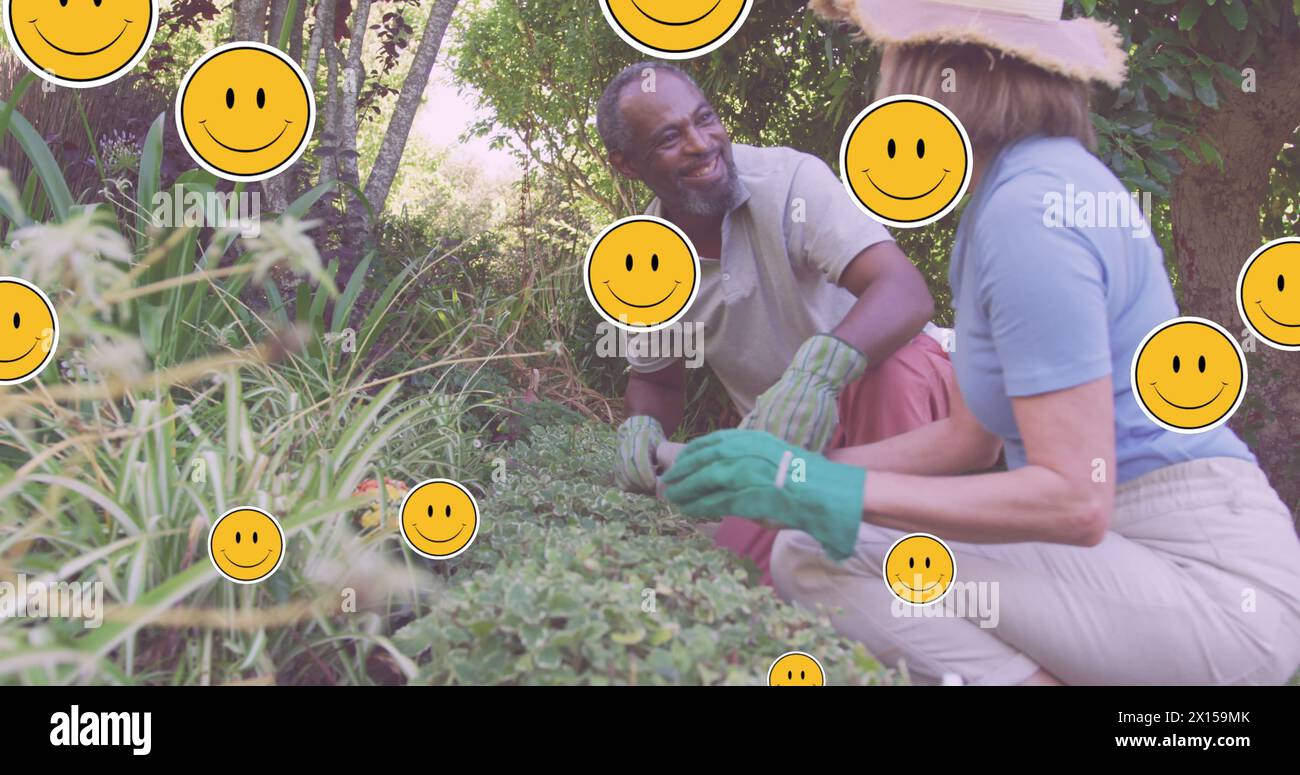 Image of emoji icons over diverse senior couple gardening Stock Photo