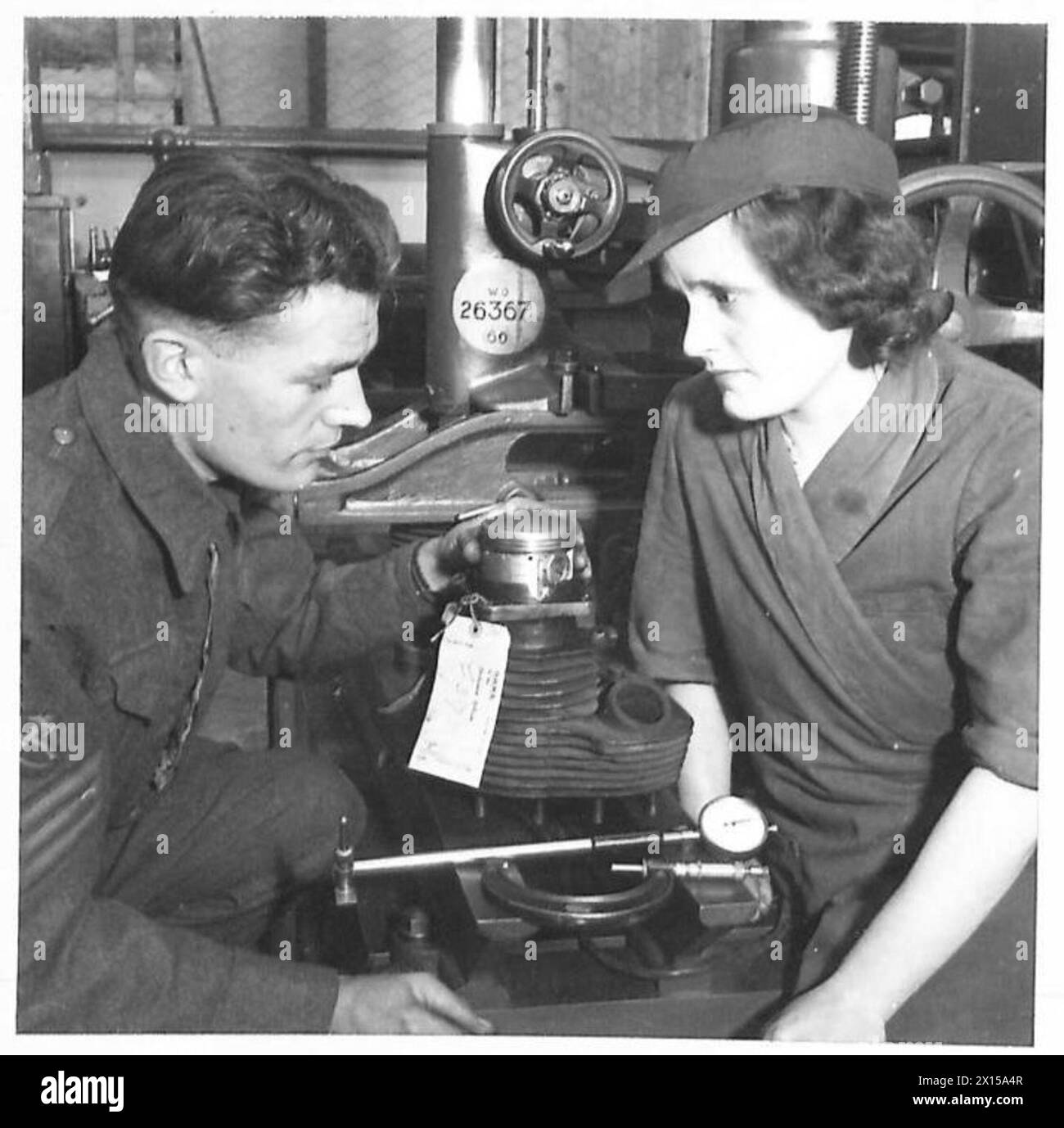 WOMEN HELP SOLDIERS IN REME WORKSHOP - Mrs. Jessie Plumb of Luton operates a Thomsen boring machine, reboring motor cycle cylinders. Mrs. Plumb is seen here with a Staff Sergeant examining a cylinder she has rebored British Army Stock Photo