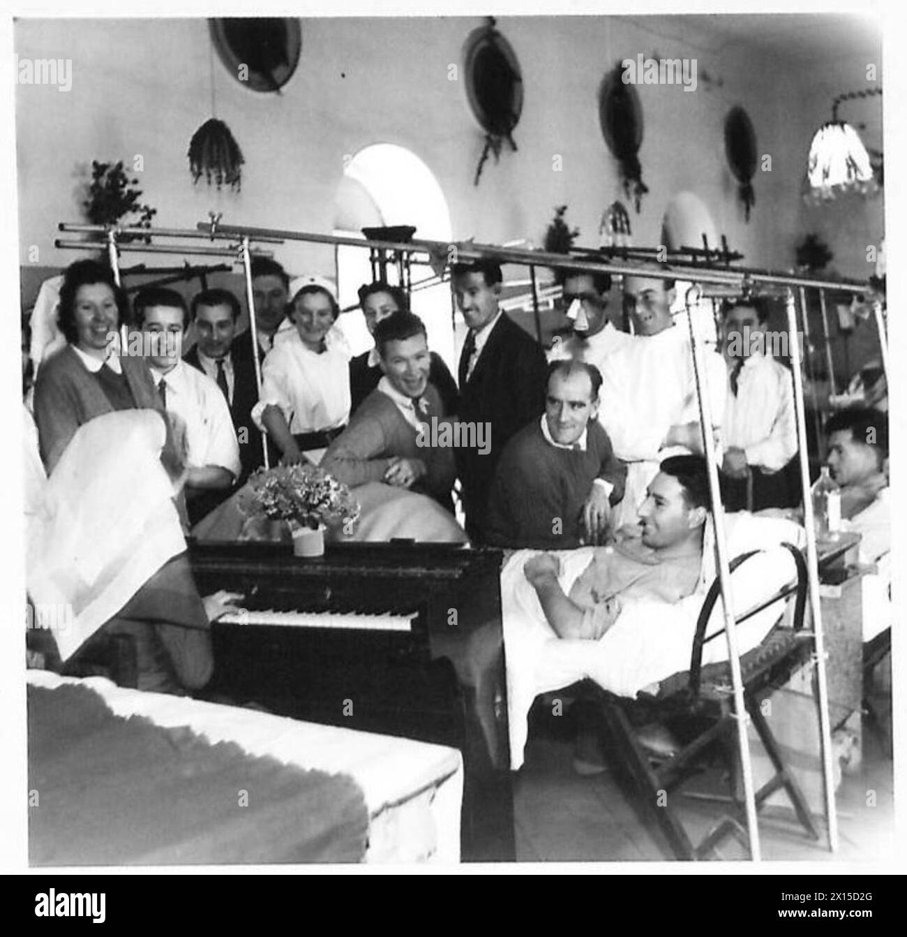 CHRISTMAS AT 104 BRITISH GENERAL HOSPITAL : OBSERVER STORY - Ward singing - left to right:- Nursing Officer M. Hawkins of Acomb, Hexham, Northumberland (seated at piano back to camera) Nursing Officer A. Ramage of Fforestfach, Swansea Pte. J. Johnstone of 12 Dewsbury Place, Longsight, Manchester VAD Iseult Passy of St.Anta, Carris Bay, Cornwall L/Cpl. F. Mayo of 20 Newhall Street, Walsall, Staffs Mountaineer T. Summers of Campbell, 183 Bolton Street, Glasgow, C.4. Pte. N. Webster of 85 Greaves Street, Little Hordon, Bradford, Yorks British Army Stock Photo
