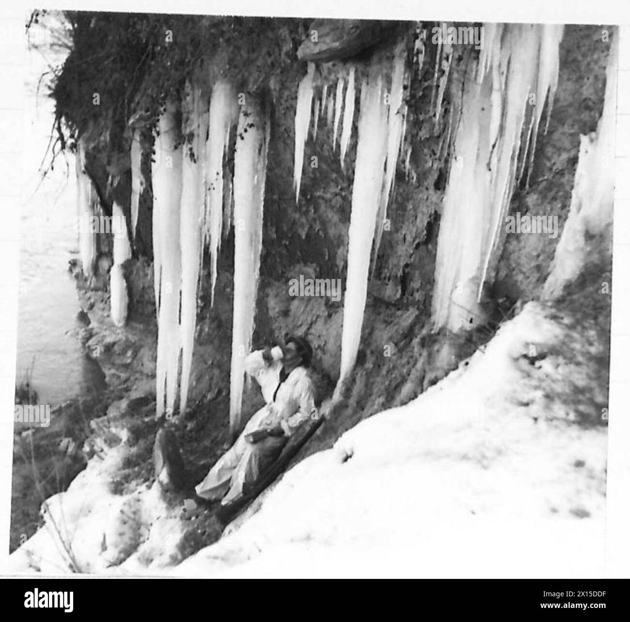 FIFTH ARMY : VARIOUS - Sapper Raymond Vass, 525 Field Sqn. R.E., of 7 Glebe Road, Crondall, near Farnham, Surrey, breaks for lunch during work on a ferry across the River Santerno. Bitter cold had produced these huge icicles. Spr. Vass wears a snowsuit whilst working, as the area ia under enemy observation from Tosignano British Army Stock Photo