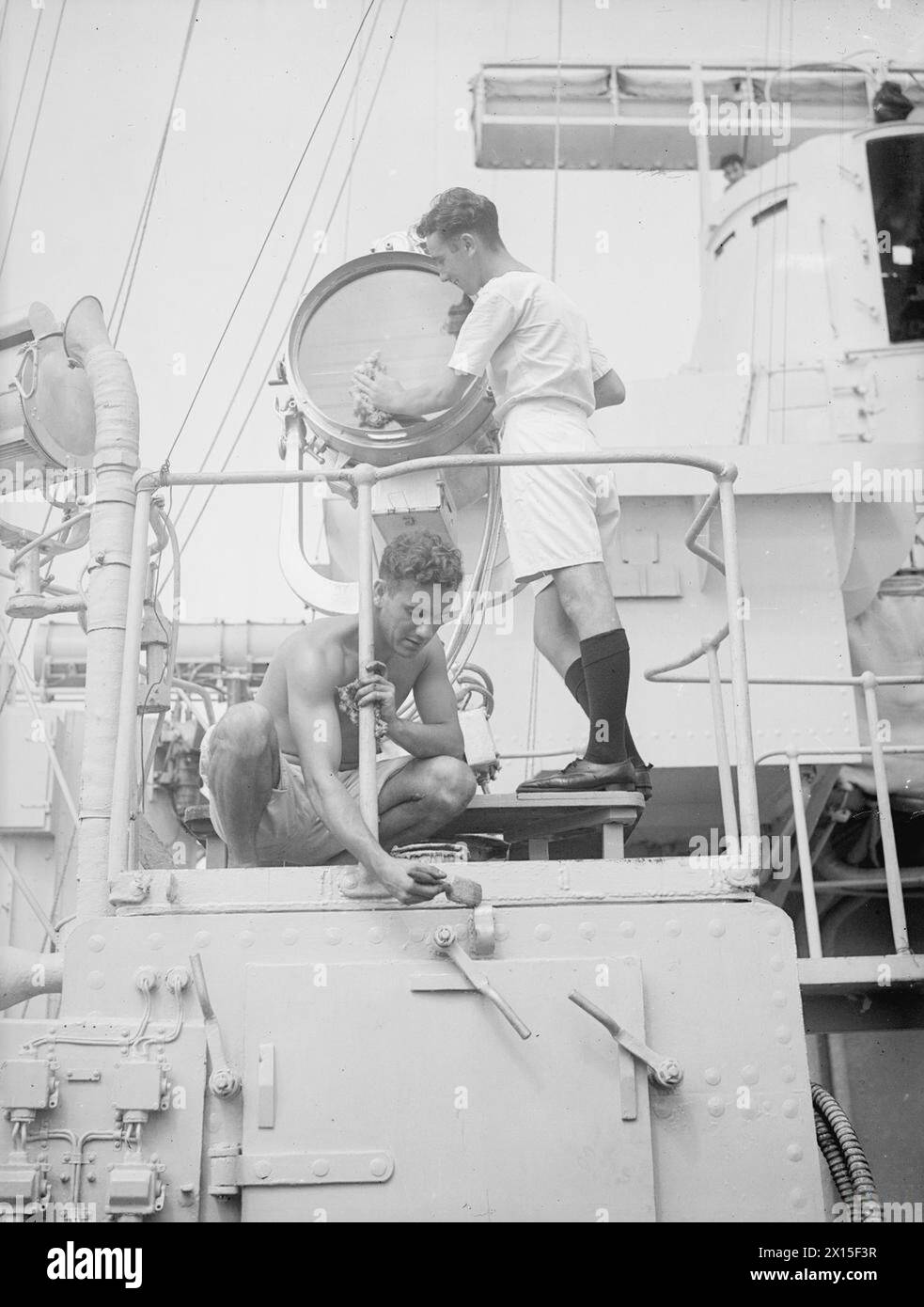 HMS LONDON SAILS FOR HOME. OCTOBER 1945, ON BOARD THE CRUISER HMS LONDON, COLOMBO, CEYLON, AND AT SEA. BEFORE SHE SAILED FROM COLOMBO TO THE UNITED KINGDOM, MEMBERS OF THE LONDON'S SHIPS COMPANY WHO WERE NOT DUE FOR RELEASE OR REPATRIATION WERE REPLACED BY MEN DUE FOR RETURN TO BRITAIN. - Homeward bound A/B George Jaques of Liecester (polishing signal projector) and A/B Edgar Oates of Mottingham, London, lend a hand to make certain that the cruiser will look her best when she sails into a home port Stock Photo