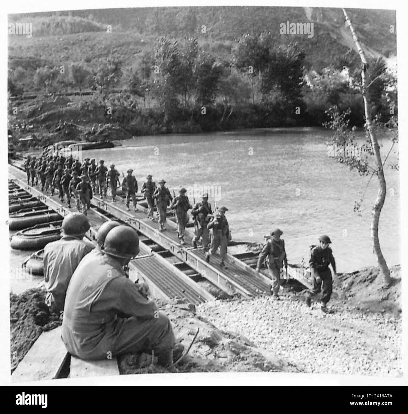 CROSSING OF THE RIVER VOLTURNO - Three American engineers watch British troops and transport crossing the bridge British Army Stock Photo