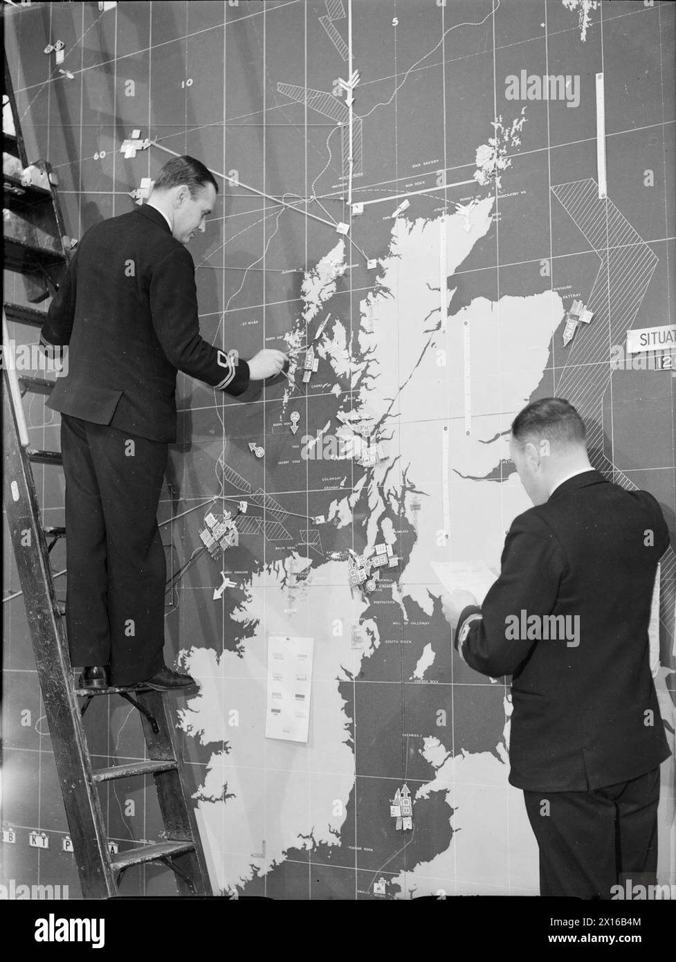 CONVOYS DURING THE SECOND WORLD WAR - Two lieutenants, one a Royal Navy Reserve the other a Royal Navy Volunteer Reserve use coded tags to plot the positions of convoys on a large wall map of the British Isles and North Atlantic. This map is in the Operations Room of Derby House, Liverpool, the home of Western Approaches Command, July 1941 Stock Photo