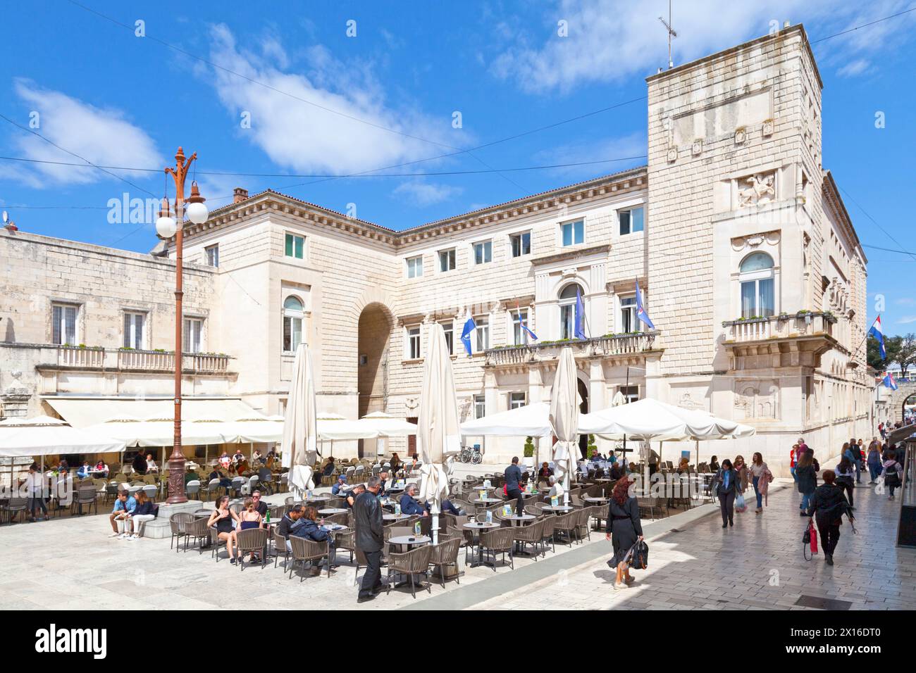 Zadar, Croatia, April 15 2019: Tourists sitting on the terrace of a cafe on the People's Square in front of the town hall. Stock Photo