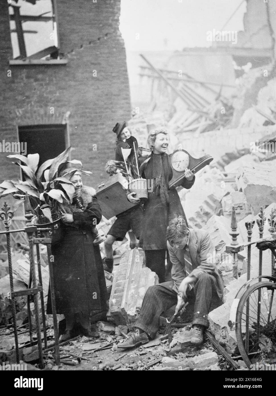 In 1940, during air raids in London, women salvaged belongings such as plants and a clock from a bomb-damaged house. Stock Photo