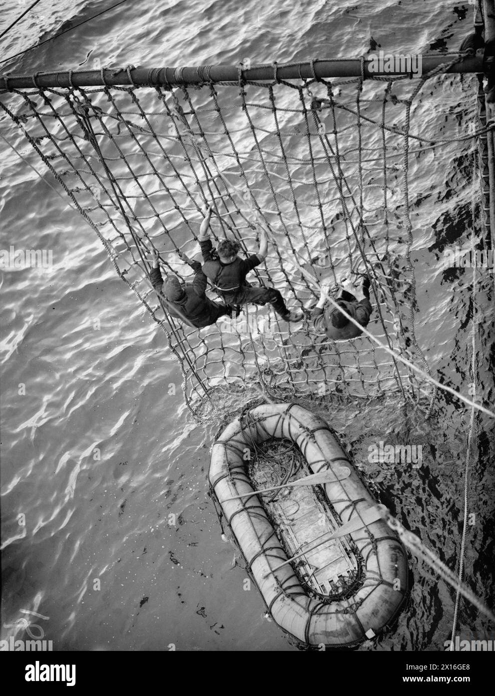 THE ROYAL NAVY DURING THE SECOND WORLD WAR - Practice in progress in the Clyde, off Greenock with the SS GOTHLAND, one of the fleet auxiliary rescue ships which sailed with convoys when the U-Boat war was at its height. 'Survivors' scrambling up the nets from their raft. The ship has a boom out each side for this purpose Stock Photo