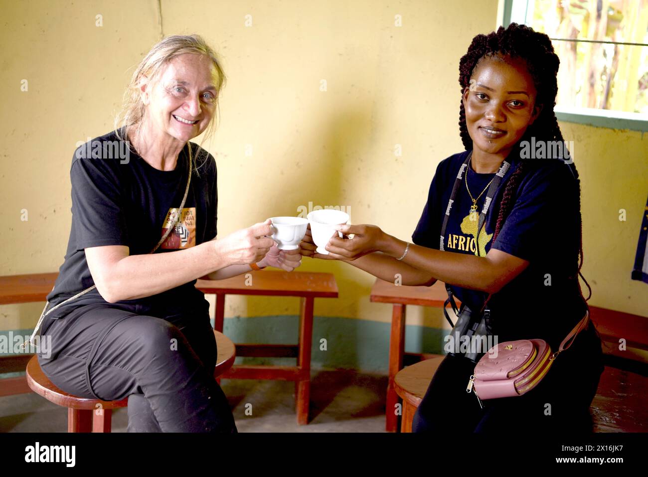In a picturesque Ugandan village, a European and a Ugandan woman engage in a heartwarming moment, toasting with freshly brewed coffee. Their connectio Stock Photo